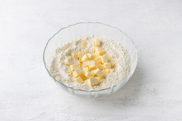 Glass bowl with flour and butter cubes on a light gray background. Cooking delicious homemade cakes step by step