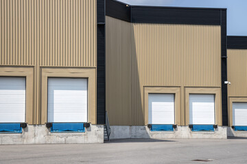 Facade of a high bay commercial building showing empty loading docks with closed metal doors, vertical corrugated metal siding, day7time, sunny, nobody