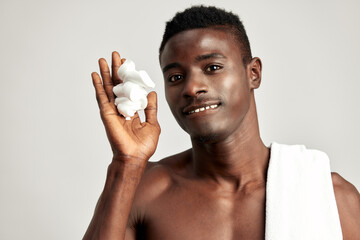 Studio portrait of handsome black guy with naked torso applying cream on his face. Afro American...