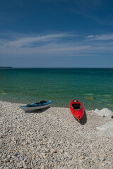 Two bright colorful kayaks on the white rocky beach by crystal clear see thru turquoise water. Sunny day, blue sky. Bruce Peninsula, Georgian Bay, Ontario, Canada.