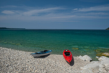 Obraz premium Two bright colorful kayaks on the white rocky beach by crystal clear see thru turquoise water. Sunny day, blue sky. Bruce Peninsula, Georgian Bay, Ontario, Canada.