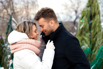 Happy couple in love in winter park. Young beautiful man and woman in winterwear embracing and looking at each other with tenderness. Romantic winter outside date.