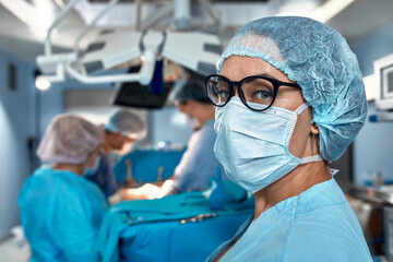 Close-up portrait of a female doctor in glasses and face mask on the background of surgeons team...
