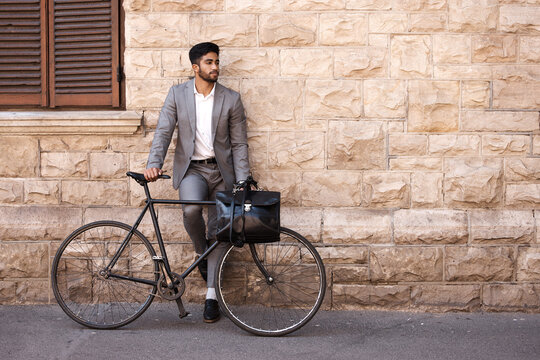Bicycle, suit and businessman in the city for travel standing by a brick wall building. Briefcase, professional and young male employee riding a bike or commuting to his work office in an urban town.