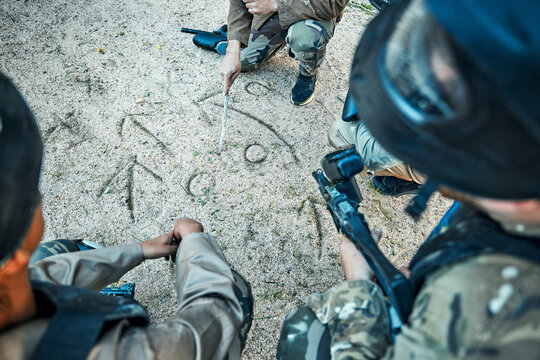 Paintball, battlefield and team building with game plan, mission and strategy drawing in sand with soldier group. War, gun and plan attack, people outdoor and military tactics and army with teamwork