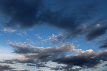 Cielo azul contrastado con nubes negras, blancas y grises con luna llena. 
