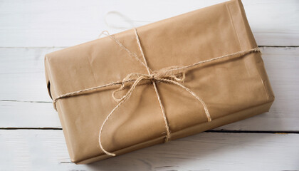 Close up Christmas style rustic brown paper package tied up with strings. White wood floor...