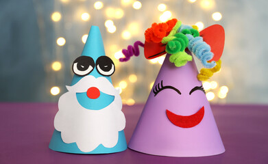 Funny handmade party hats on purple table against blurred lights, closeup