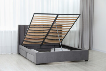 Modern bed with storage space for bedding under lifted slatted base in room