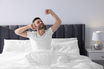 Handsome man stretching in soft bed at home in morning