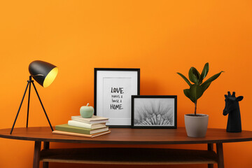 Wooden coffee table with different decor near orange wall indoors. Stylish interior design