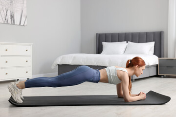 Young woman in sportswear doing exercises on fitness mat in bedroom - obrazy, fototapety, plakaty