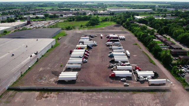 overview of yard parking lot with semi trucks and trailers - reefers, dry van, flatbeds, stingers, bob tails. Truck Driver is entering yard while another is leaving. Plainfield Illinois USA