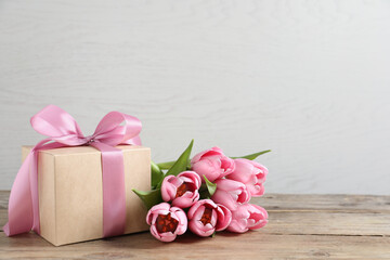 Gift box and beautiful tulip flowers on wooden table, space for text