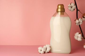 Bottle of fabric softener and fluffy cotton flowers on pink background, space for text