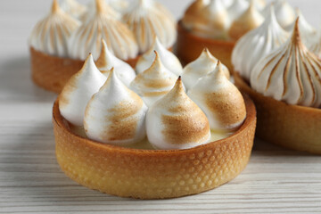 Many different tartlets with meringue on white wooden table, closeup. Tasty dessert
