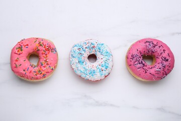 Sweet glazed donuts decorated with sprinkles on white marble table, flat lay. Tasty confectionery