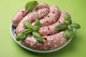 Raw homemade sausages, basil leaves and peppercorns on green table, closeup