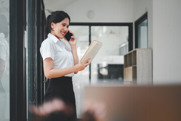 Fototapeta premium Happy businesswoman talking on mobile phone while analyzing weekly schedule in her paper.