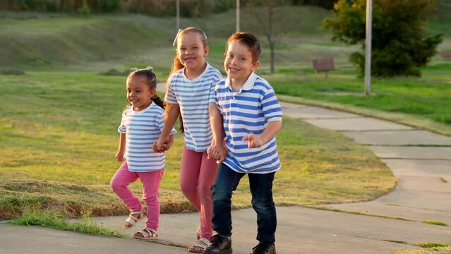 Tres niños hermanos amigos latinos felices subiendo el camino caminando de frente por la via calle sendero del parque en verano vestidos similares al aire libre en el atardecer al exterior