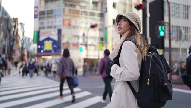 Young Asian woman walking on city street crosswalk and looking cityscape building in Tokyo, Japan. Attractive girl traveler enjoy urban outdoor lifestyle travel in Japan on winter holiday vacation.