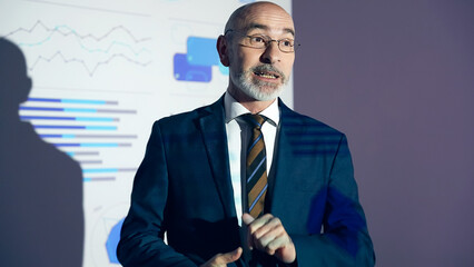 A middle-aged Caucasian business person giving a presentation using a projector screen.