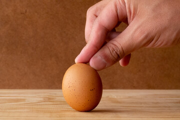 a man's hand leaving an egg standing, distinctive for its stains, on a wood, with a simple rustic style