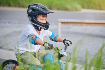 Cute little 7 years old school boy child in safety helmet wearing knee pads, elbow pads and cycling...