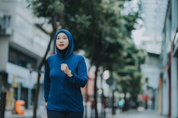 Glad smiling young asian muslim woman in hijab with fitness tracker running on building background outdoor. Fitness outside, jogging in morning, body and health care, training, concept muslim sport.