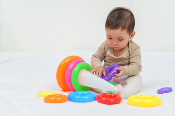 infant baby playing the pyramid toy with colored rings on bed