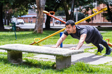 in the neighborhood park a Colombian man exercises with a set of push-ups using a bench