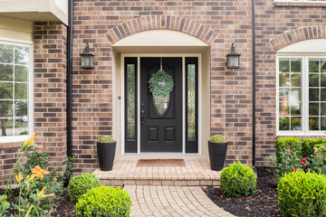 The front door of a brick home with a black front door and a stone path sidewalk. - obrazy, fototapety, plakaty