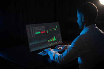 Caucasian man sits in the dark in front of a virtual screen. Stock exchange charts.