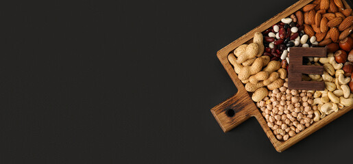 Board with different healthy nuts and beans rich in vitamin E on dark background with space for text