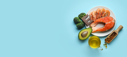 Plate with healthy products rich in vitamin E and pills on light blue background with space for text