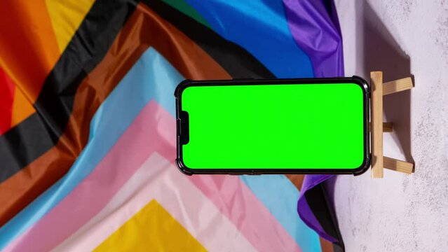 Vertical Zoom in out Mobile phone with chroma key on Rainbow LGBTQIA flag made from silk material background. Happy pride month. Symbol of LGBTQ pride month. Equal rights. Peace and freedom. Support