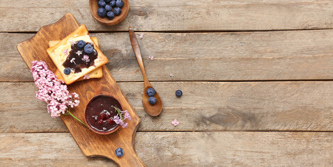 Board with sweet blueberry jam toasts and flowers on wooden background with space for text