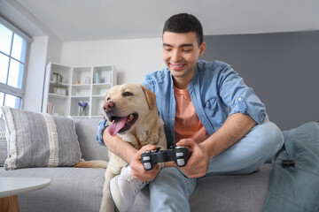 Young man with cute Labrador dog playing video game at home