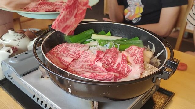 Waitress cooking Sukiyaki, a Japanese traditional food served in a hotpot for customers