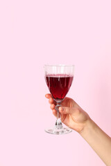 Female hand holding glass of red wine on pink background