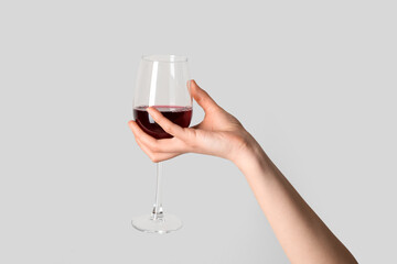 Female hand holding glass of red wine on grey background