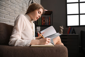 Young businesswoman reading book and making notes in office