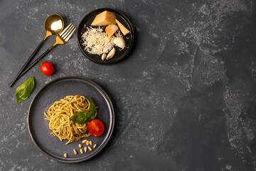 Plate with tasty pesto pasta and tomatoes on dark grunge background