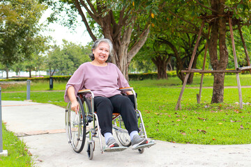 Asian elderly woman Riding a wheelchair in an outdoor park. The concept of happy retirement and health insurance for the elderly