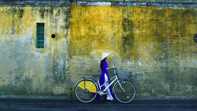 Asian woman wearing vietnam culture traditional and rolls a bicycle at Hoi an, Vietnam.