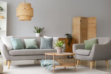 Interior of stylish living room with grey sofa, armchair and houseplant on coffee table