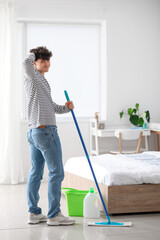 Young man mopping floor in bedroom