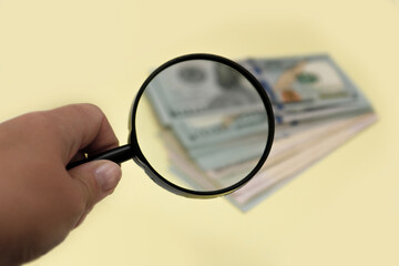 Fototapeta premium hand holding a magnifying glass over a blurred stack of banknotes