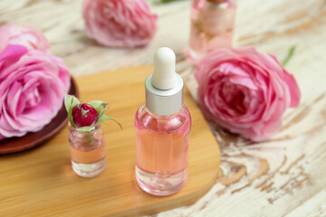 Obraz na płótnie Canvas Bottles of cosmetic oil with rose extract and flowers on light wooden table