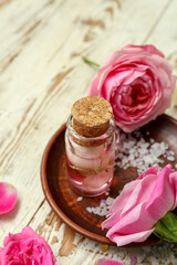 Fototapeta na wymiar Bottle of cosmetic oil with rose extract and flowers on light wooden table